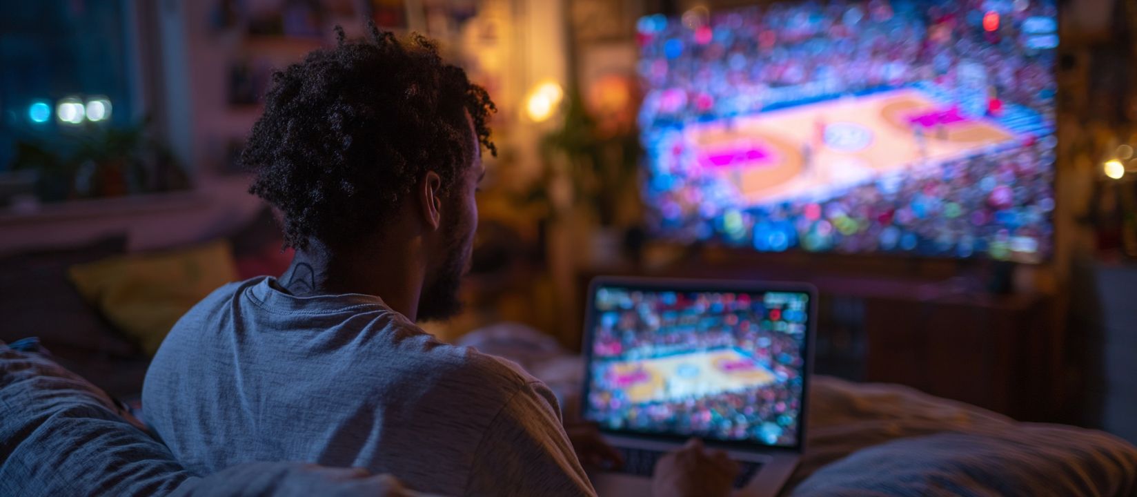 Man watching a basketball game on a big screen while placing bets online, symbolizing sports betting at 7Z777 Casino